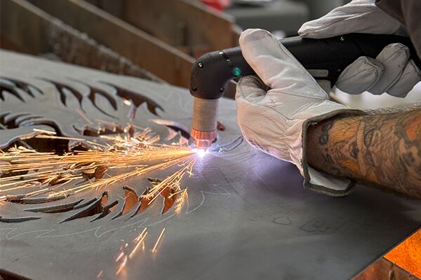 Nahaufnahme eines handgeführten Plasmabrenners beim Schneiden einer Metallplatte. Am Schnitt entstehen Funken.